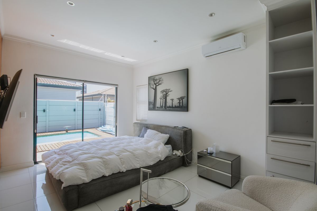 Modern bedroom featuring tiled flooring, built-in shelving, and a split-system air conditioner, with direct access to a private patio and swimming pool area.