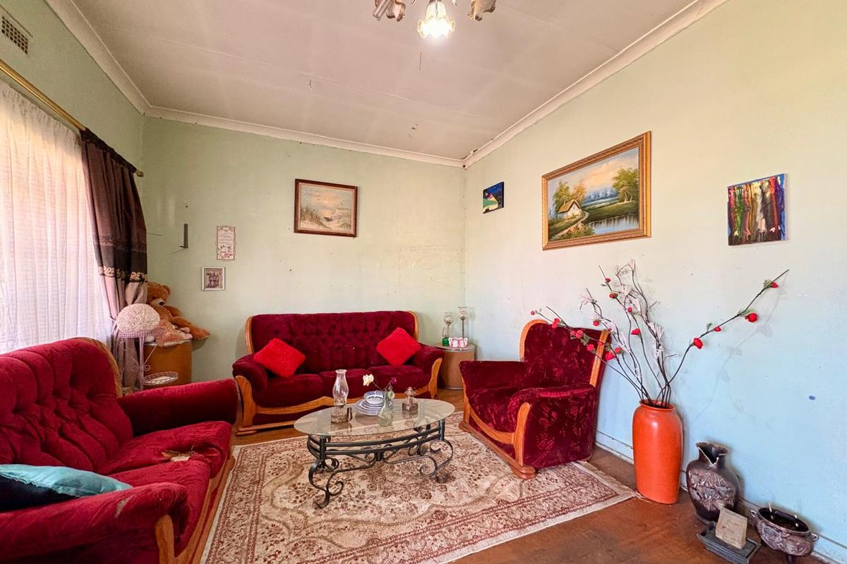 A living room featuring timber flooring, coving, and a ceiling rose, currently requiring cosmetic updates to the wall finishes.