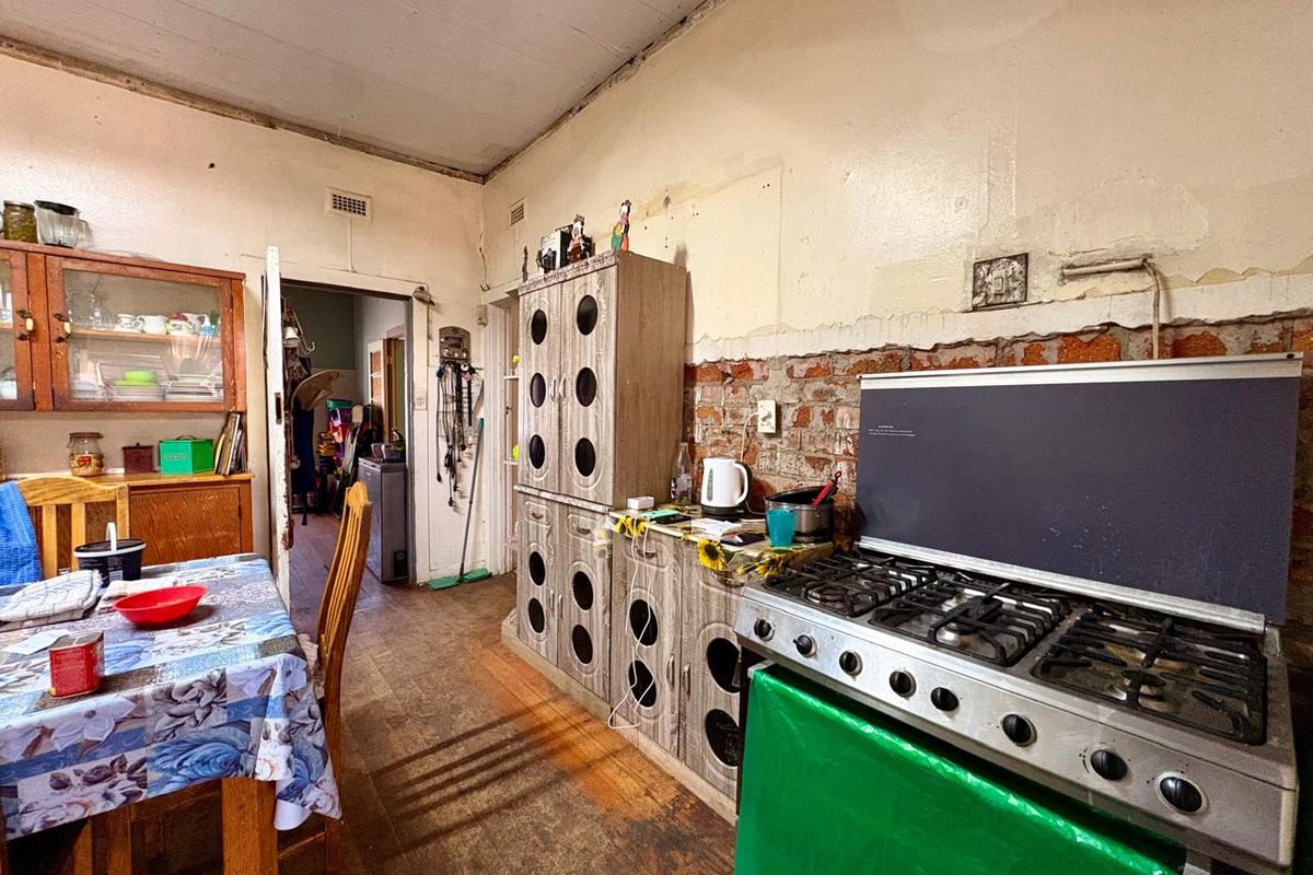 A kitchen area featuring a gas stove, built-in cabinetry, and exposed brickwork, currently requiring significant renovation and cosmetic updates to improve its condition.