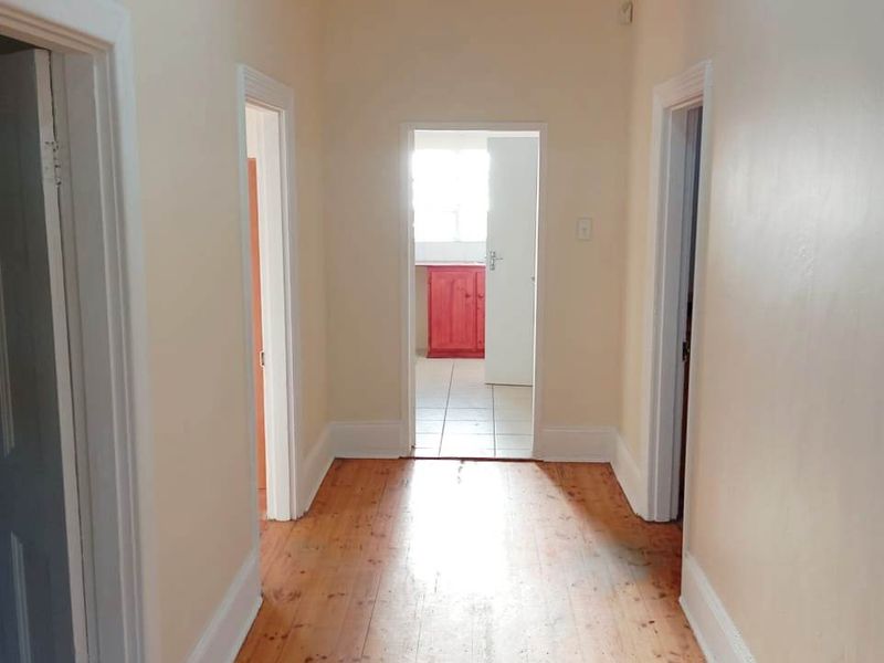 A bright, empty hallway featuring original timber flooring, classic skirting boards, and neutral wall finishes, providing access to multiple rooms.