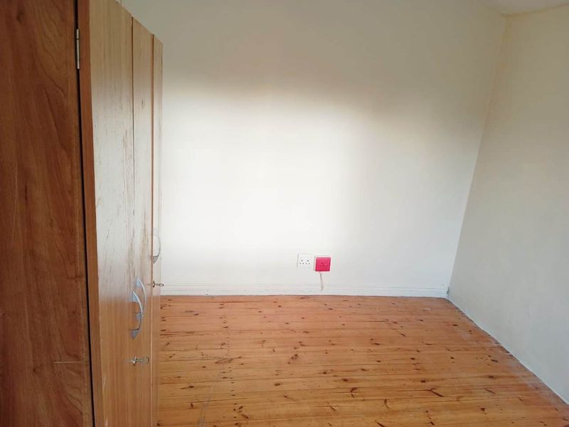 A bedroom featuring timber flooring and a built-in wooden wardrobe, providing a functional space with neutral wall finishes.