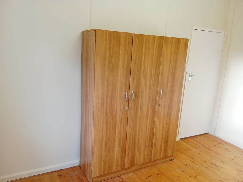 A bedroom featuring timber flooring and a freestanding wooden wardrobe.