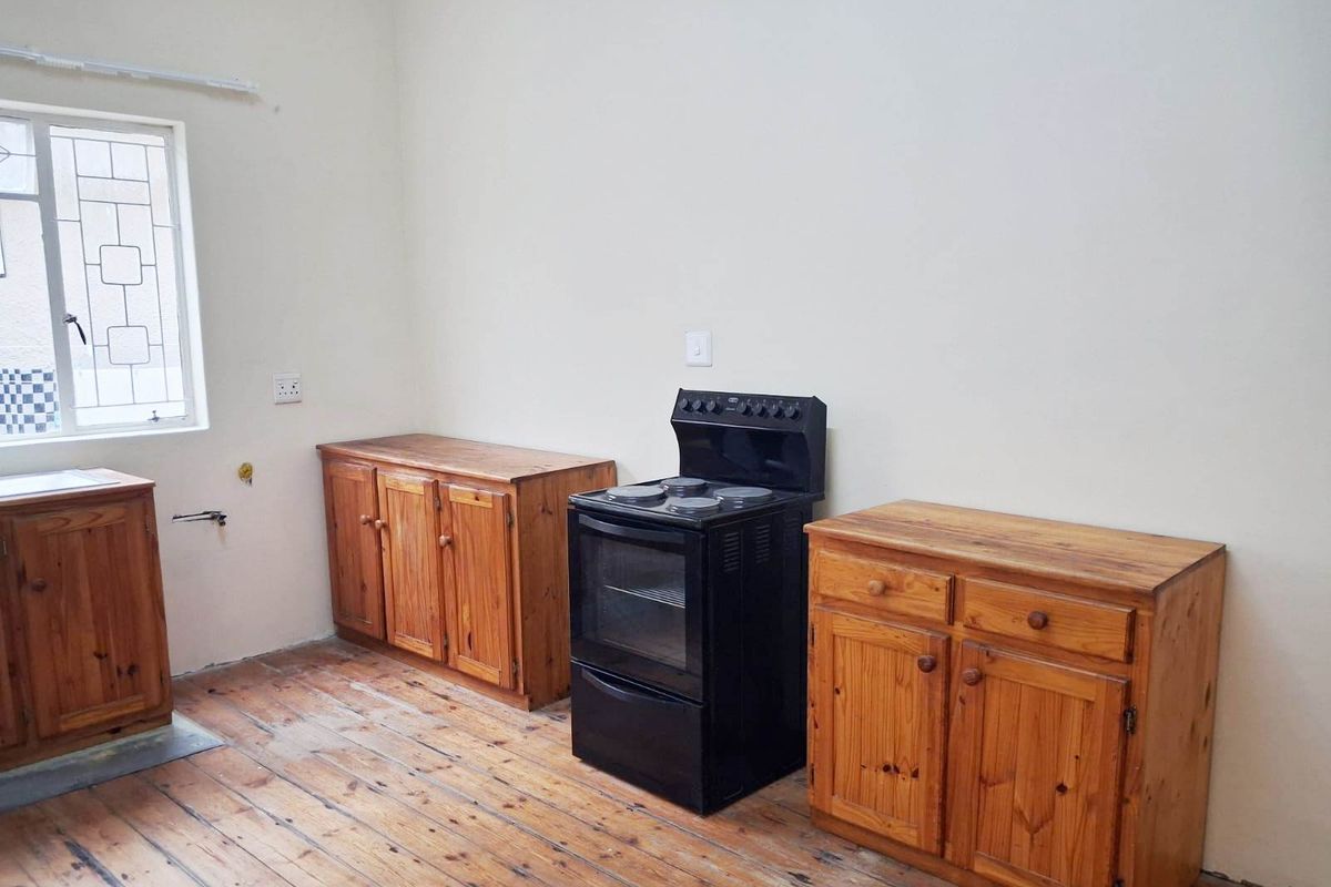 A basic kitchen area featuring timber cabinetry, a freestanding electric stove, and original timber flooring, offering a blank canvas for renovation.