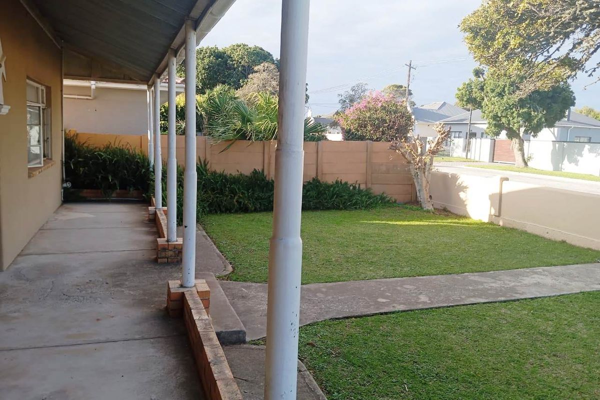 A covered patio area featuring concrete flooring and support columns, overlooking a private garden with a boundary wall.