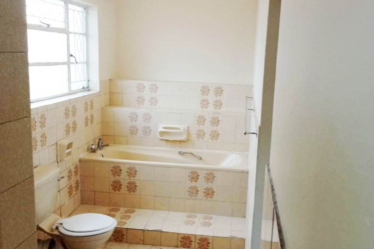 A dated bathroom featuring a built-in bathtub, ceramic wall and floor tiles, and a standard toilet, offering potential for a modern renovation.