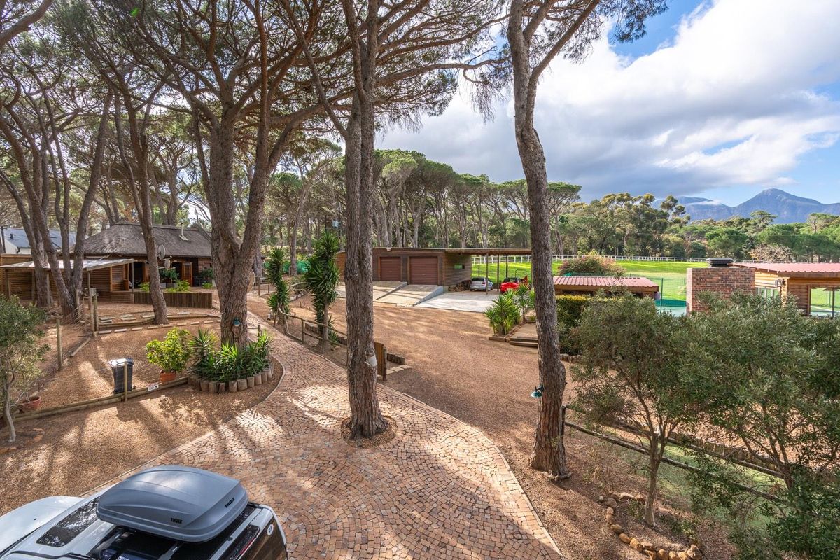 An elevated view of the farm property grounds, featuring a paved driveway, mature trees, outbuildings, and a garage area set against a scenic landscape.