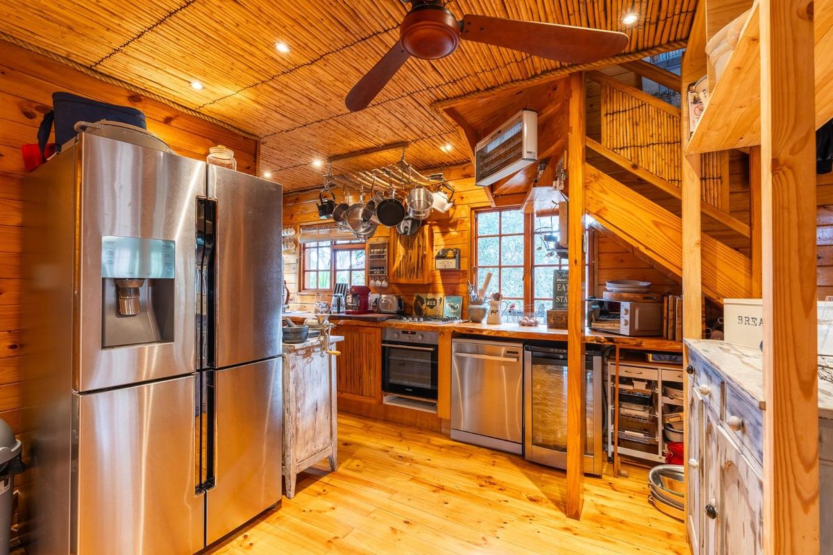 Rustic timber-clad kitchen featuring wooden cabinetry, integrated stainless steel appliances, a ceiling fan, and a staircase leading to an upper level.