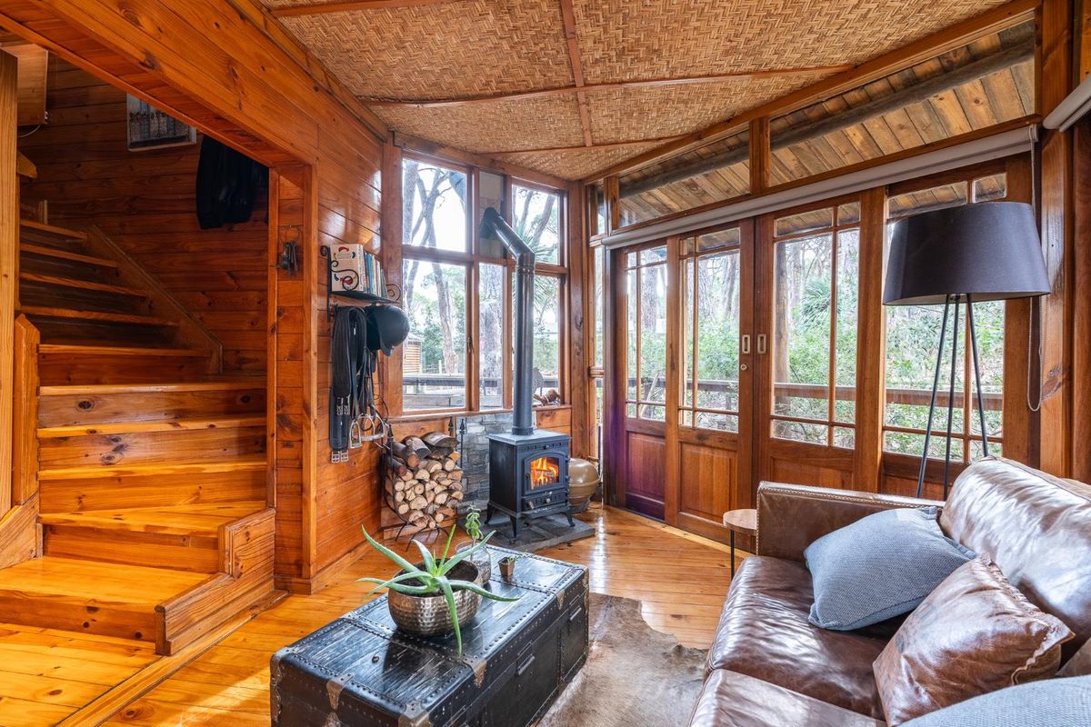 Cozy living area featuring warm timber wall paneling, a wood-burning stove, and direct access to an outdoor deck through large glass doors.