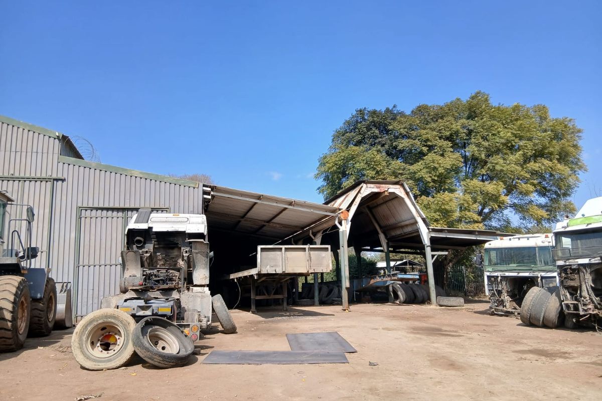An industrial utility shed area with corrugated metal roofing and steel framing, currently used for storage and vehicle maintenance on the small holding.