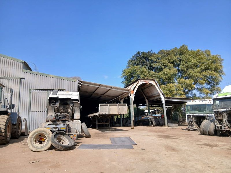 An industrial utility shed area with corrugated metal roofing and steel framing, currently used for storage and vehicle maintenance on the small holding.