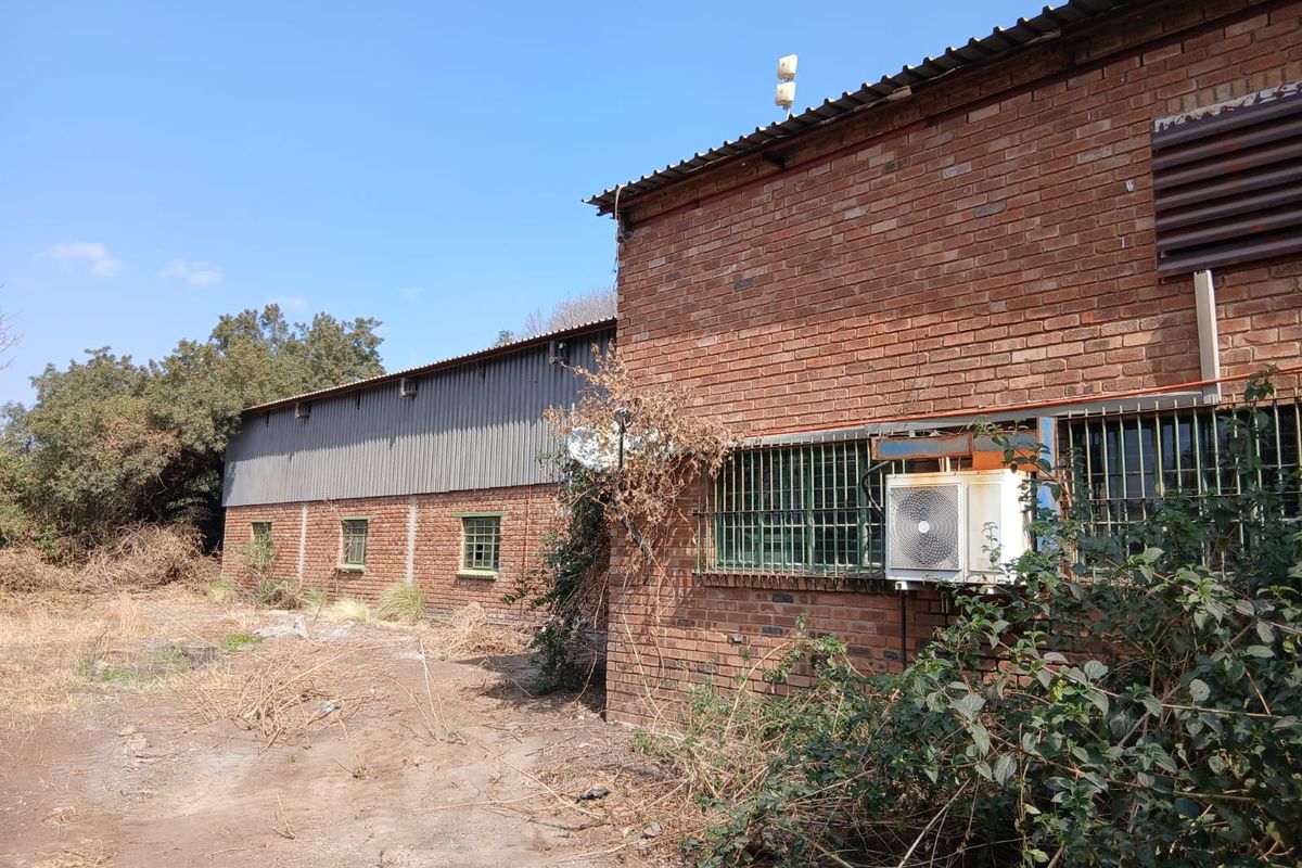 Rear exterior view of a face brick building featuring corrugated metal roofing, security bars on windows, and an external air conditioning unit.