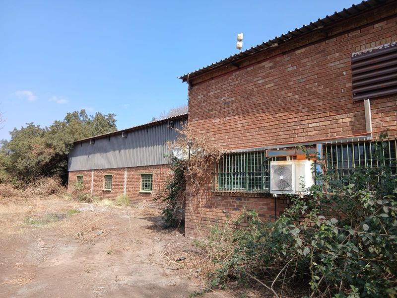 Rear exterior view of a face brick building featuring corrugated metal roofing, security bars on windows, and an external air conditioning unit.