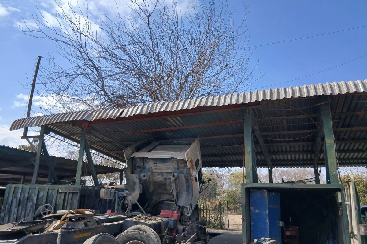 An open-sided utility shed with a corrugated iron roof and steel support structure, currently used for vehicle maintenance and storage.