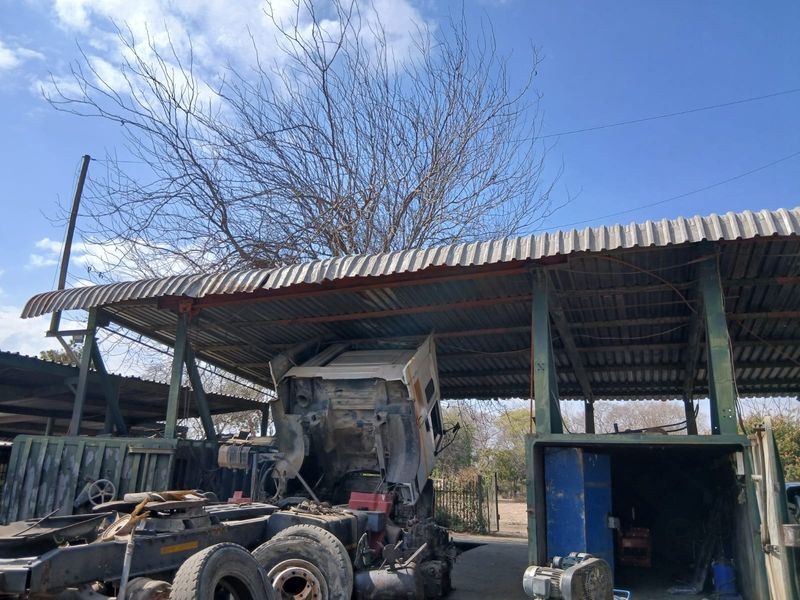 An open-sided utility shed with a corrugated iron roof and steel support structure, currently used for vehicle maintenance and storage.