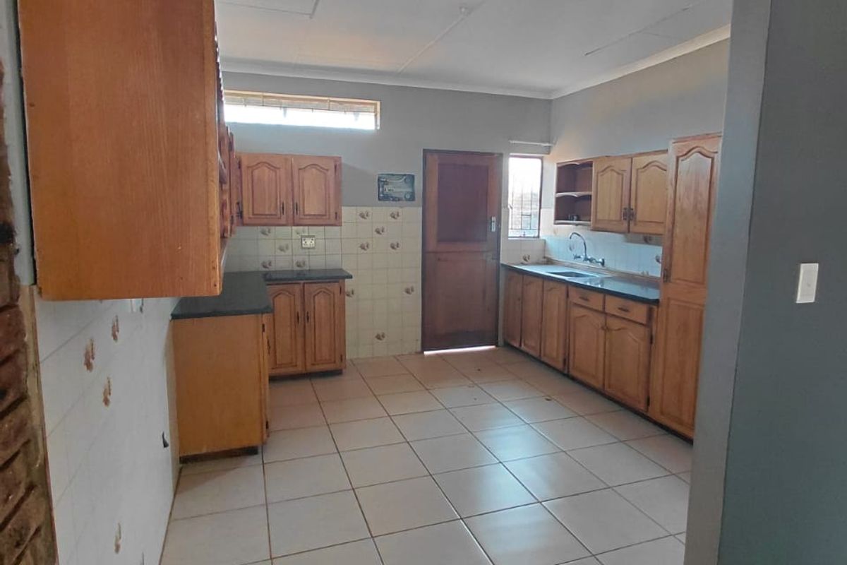 A functional kitchen featuring wooden cabinetry, tiled flooring, and a double sink, offering a practical layout with potential for modern updates.