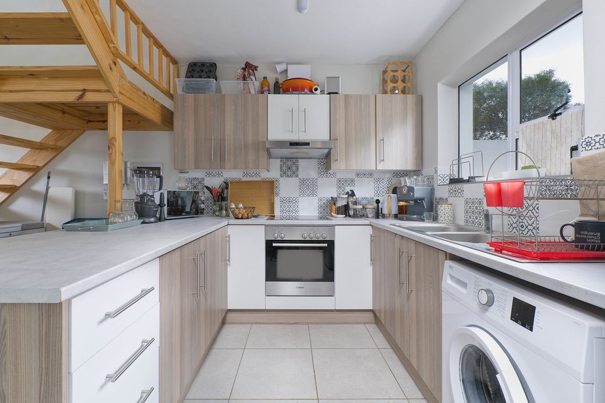 Compact U-shaped kitchen featuring modern cabinetry, built-in oven, extractor fan, tiled backsplash, and integrated laundry facilities, adjacent to a timber staircase.