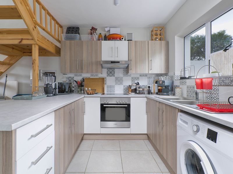 Compact U-shaped kitchen featuring modern cabinetry, built-in oven, extractor fan, tiled backsplash, and integrated laundry facilities, adjacent to a timber staircase.