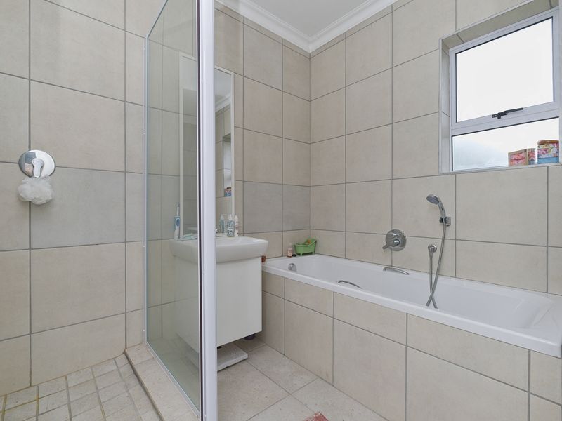 A clean, functional bathroom featuring a tiled shower enclosure, a built-in bathtub, and a vanity basin with neutral wall and floor tiling.
