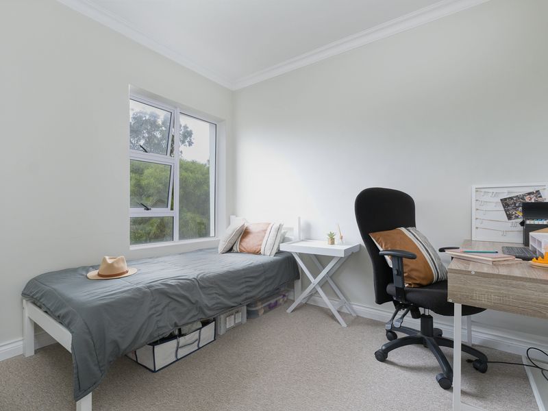 A bright and well-maintained bedroom featuring neutral walls, carpet flooring, and a large window providing natural light.