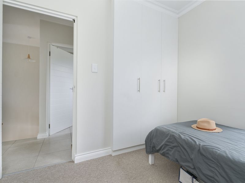 A clean, neutral bedroom featuring built-in cupboards, carpeted flooring, and classic cornice detailing, offering a bright and functional living space.