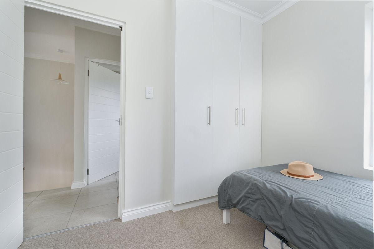 A clean, neutral bedroom featuring built-in cupboards, carpeted flooring, and classic cornice detailing, offering a bright and functional living space.