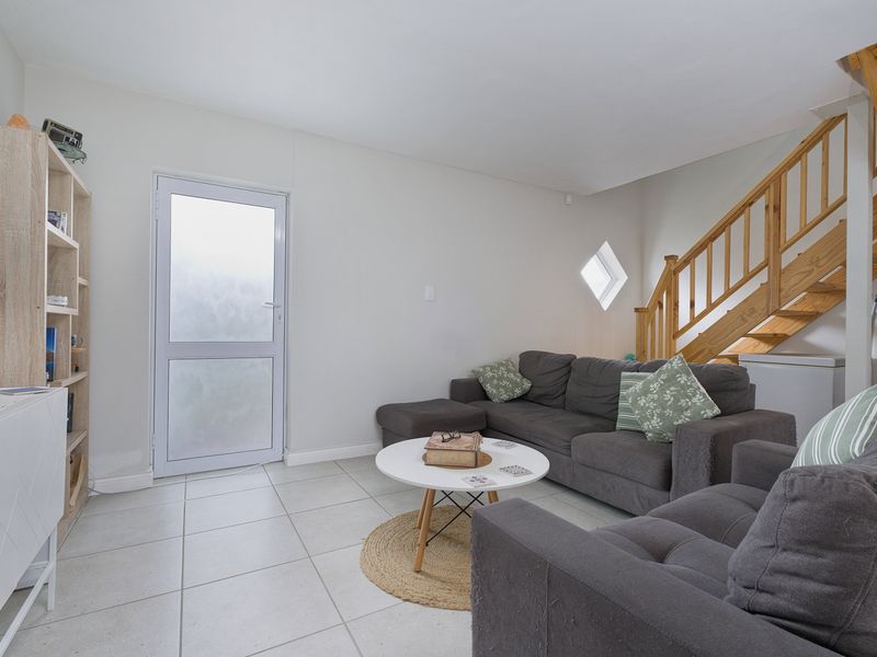 A living room featuring tiled flooring, a wooden staircase, and a frosted glass exterior door with a unique diamond-shaped window.