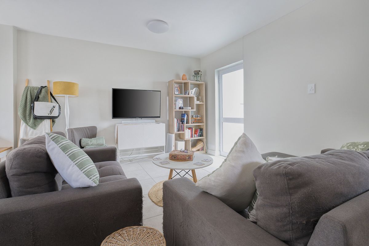 A bright and comfortable living room featuring neutral tiled flooring and a glass door providing natural light and access to the exterior.