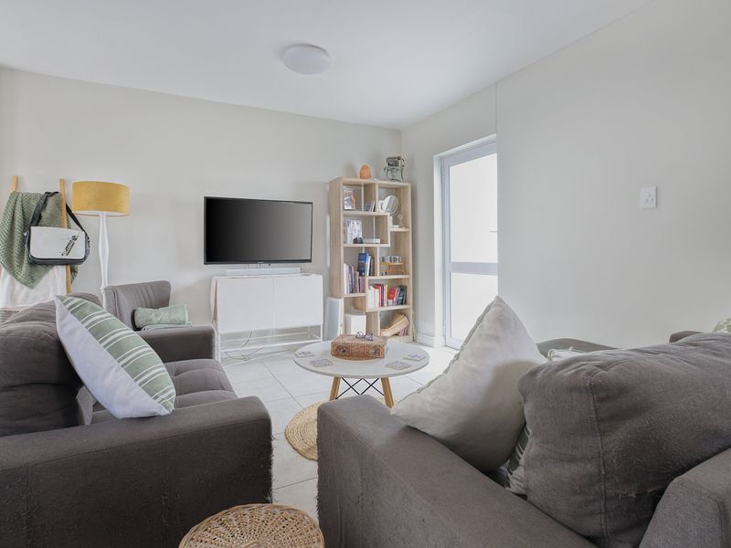 A bright and comfortable living room featuring neutral tiled flooring and a glass door providing natural light and access to the exterior.