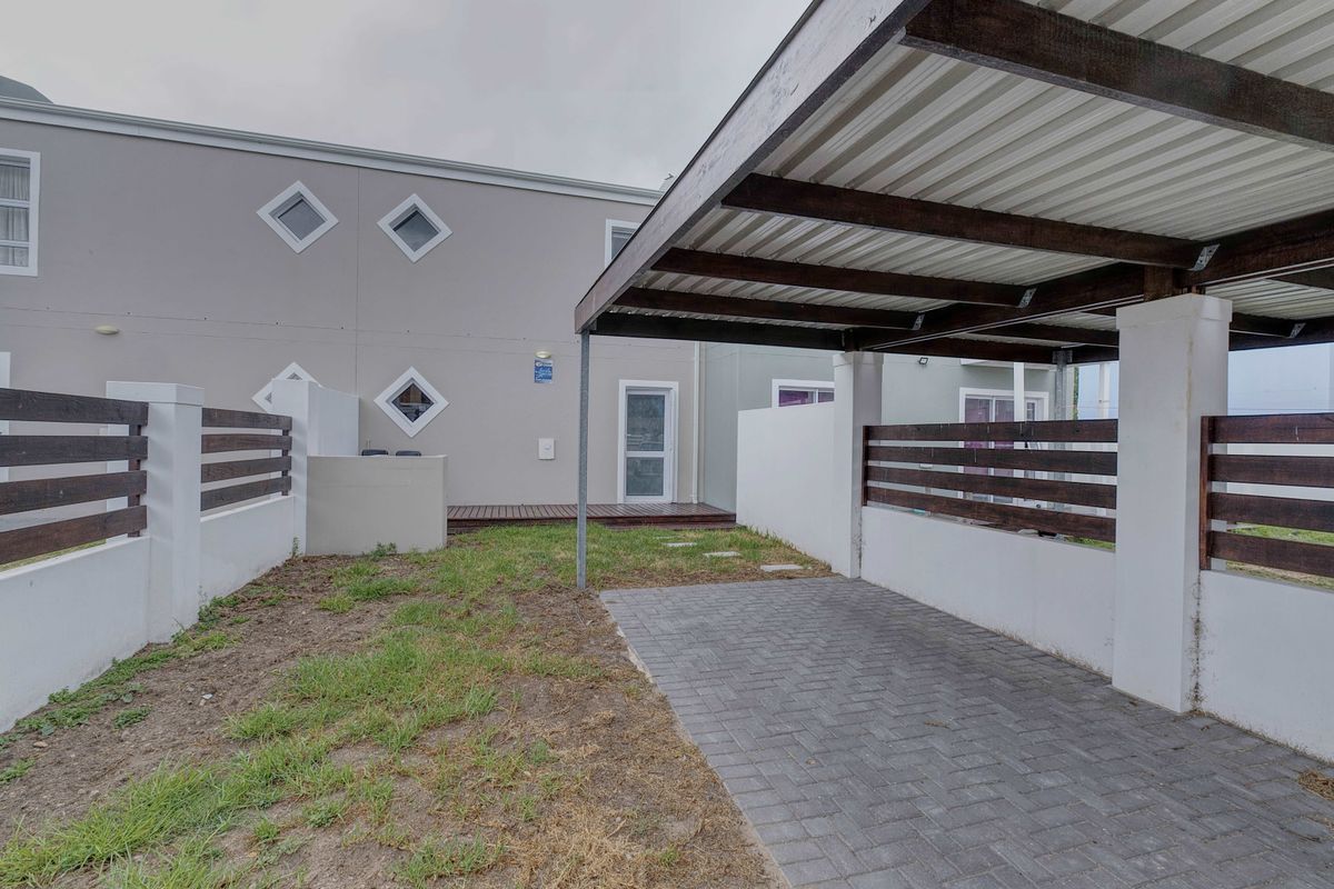 Rear exterior area featuring a covered carport, paved driveway, timber slat fencing, and a small timber deck leading to the house entrance.