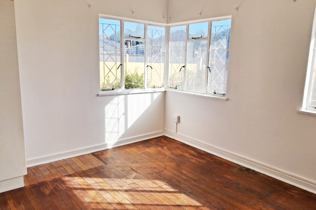 A bright, empty bedroom featuring original hardwood timber flooring and charming corner windows with leaded glass detailing.