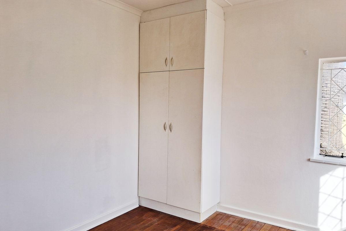 An empty bedroom featuring original timber flooring, a built-in cupboard, and a classic leaded glass window.
