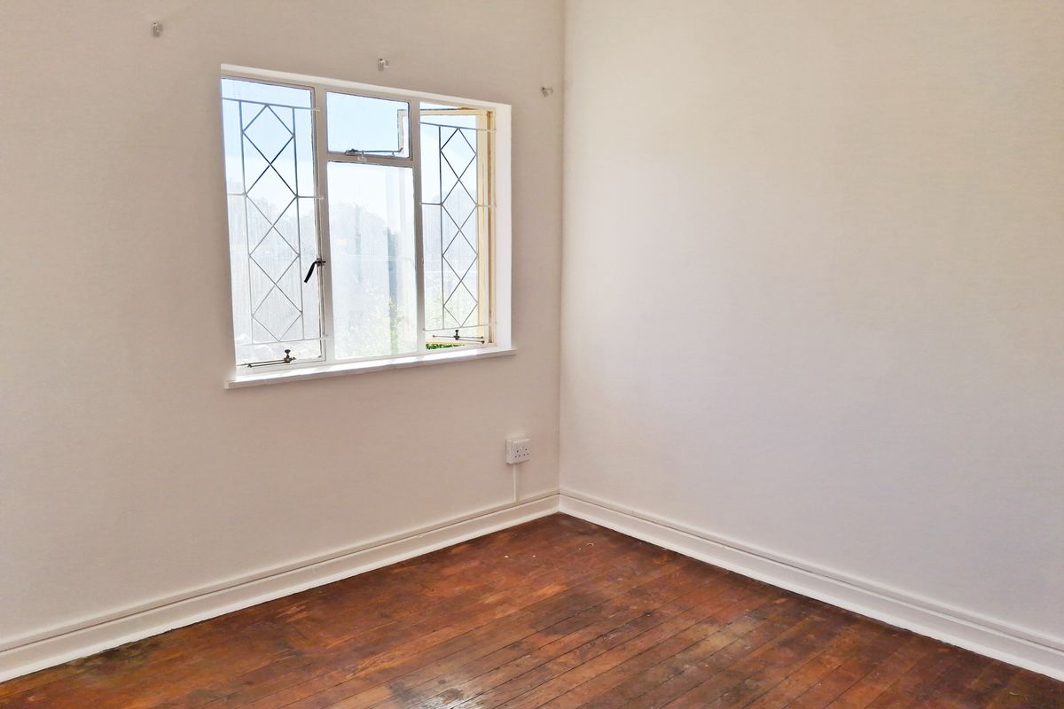 An empty bedroom featuring original timber flooring, white walls, and a window with integrated security bars.