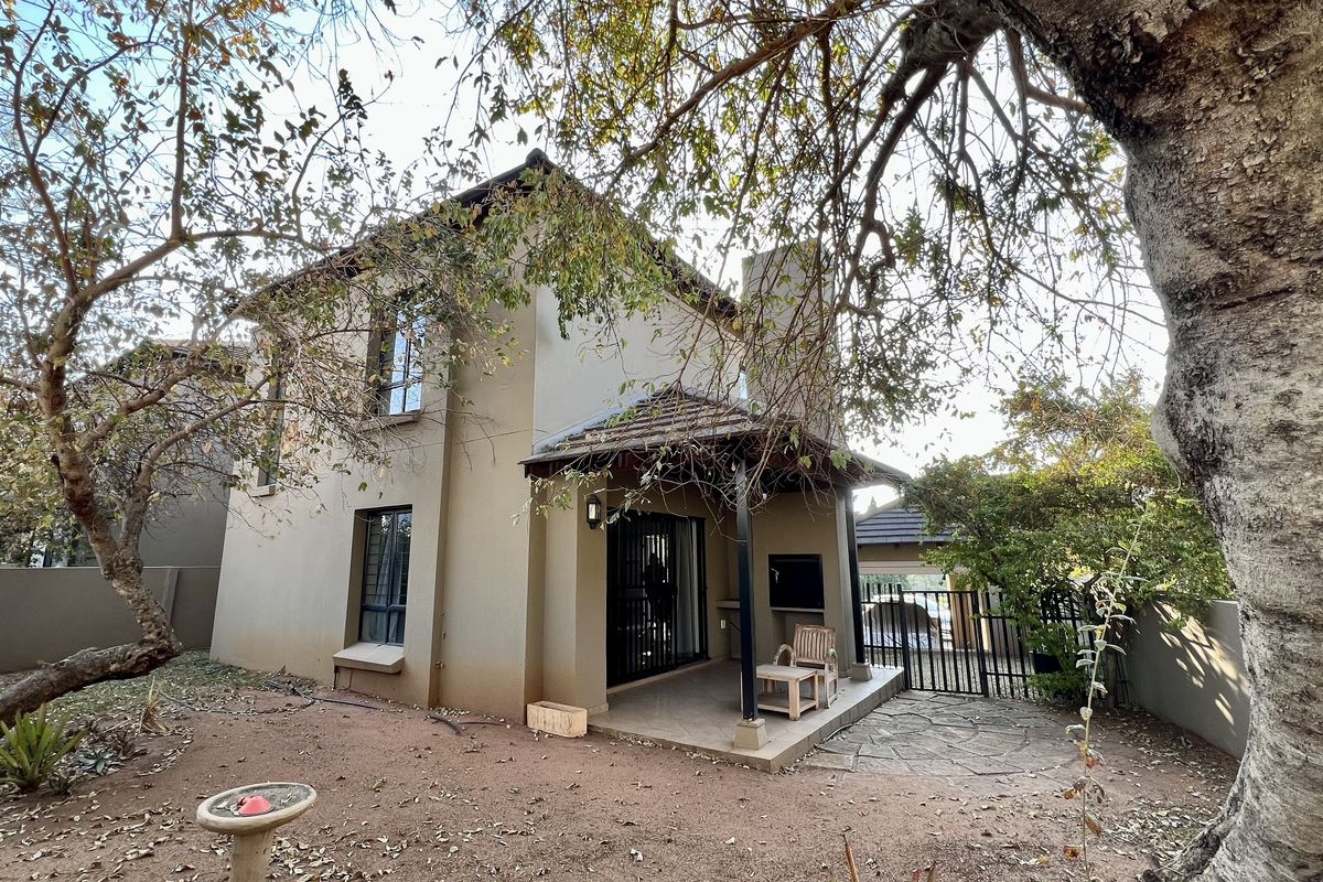 Rear view of a two-story house featuring a covered patio with a built-in braai, set within a private garden area.