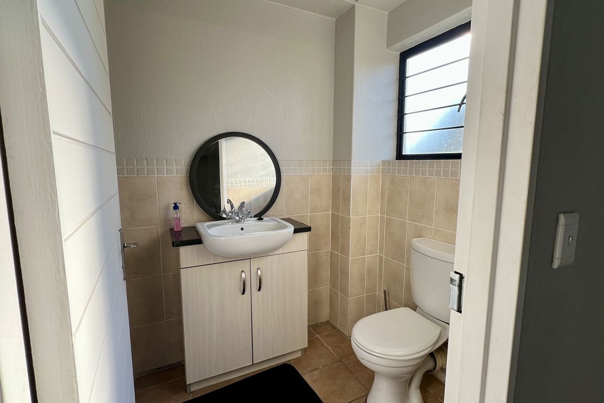A compact bathroom featuring a vanity with a basin, a toilet, and tiled walls with a window for natural light.