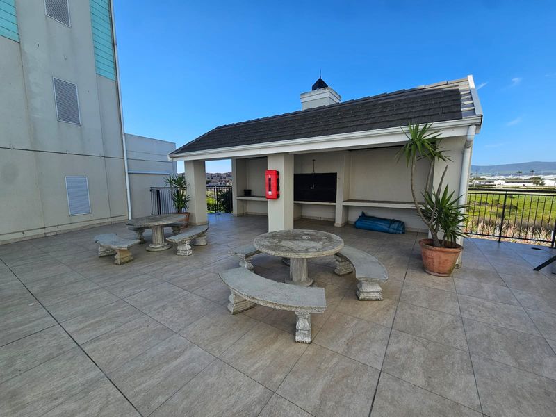 A spacious covered outdoor patio area featuring tiled flooring, a built-in braai, and fixed stone seating, ideal for communal outdoor entertaining.