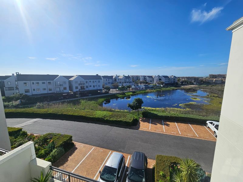 Elevated view overlooking the complex parking area, landscaped gardens, and a natural wetland pond.