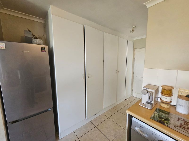 Kitchen area featuring extensive built-in white cabinetry, tiled flooring, and a functional workspace with a tiled backsplash and integrated dishwasher.