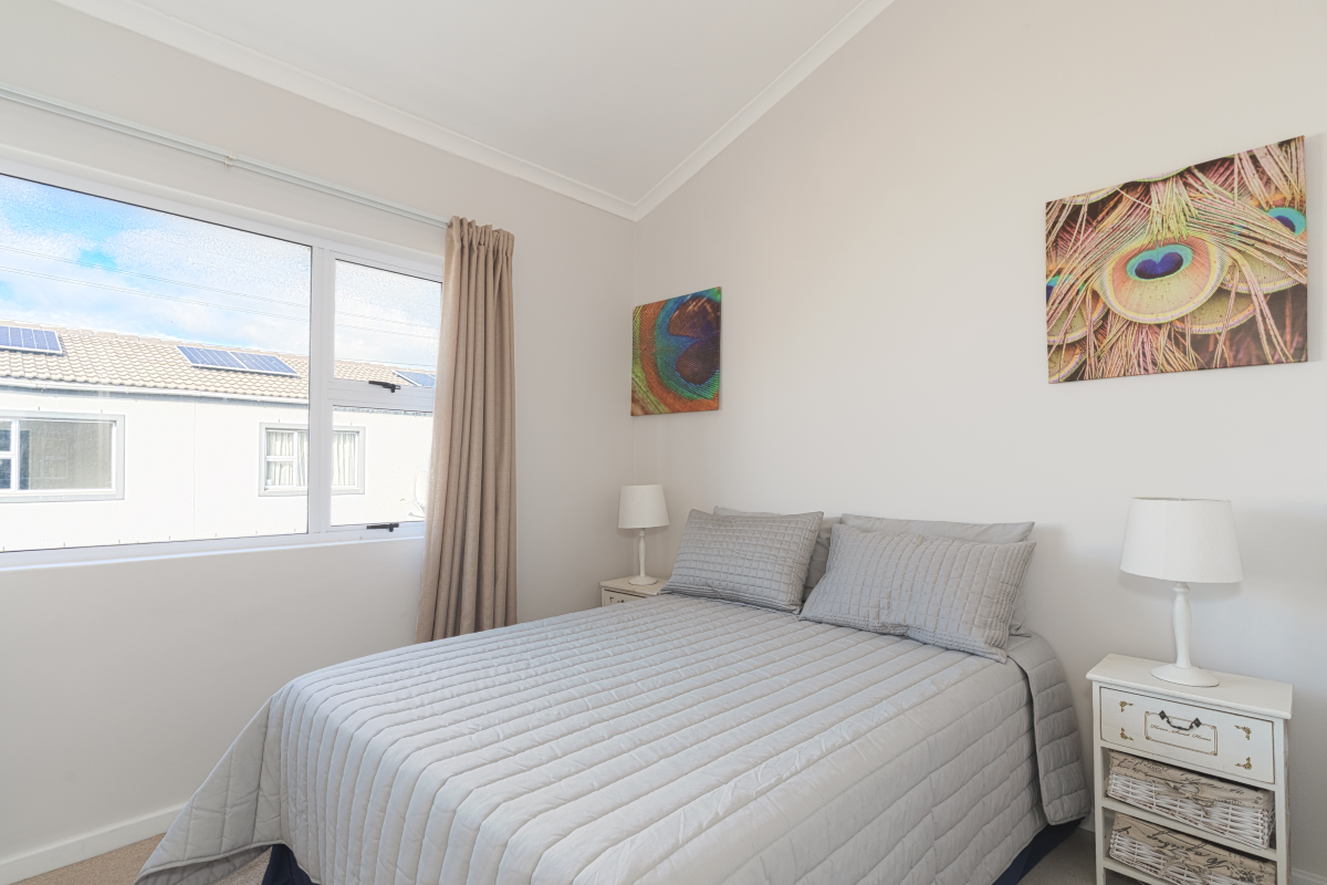 A bright and well-maintained bedroom featuring a vaulted ceiling, neutral wall finishes, and a large window providing natural light.