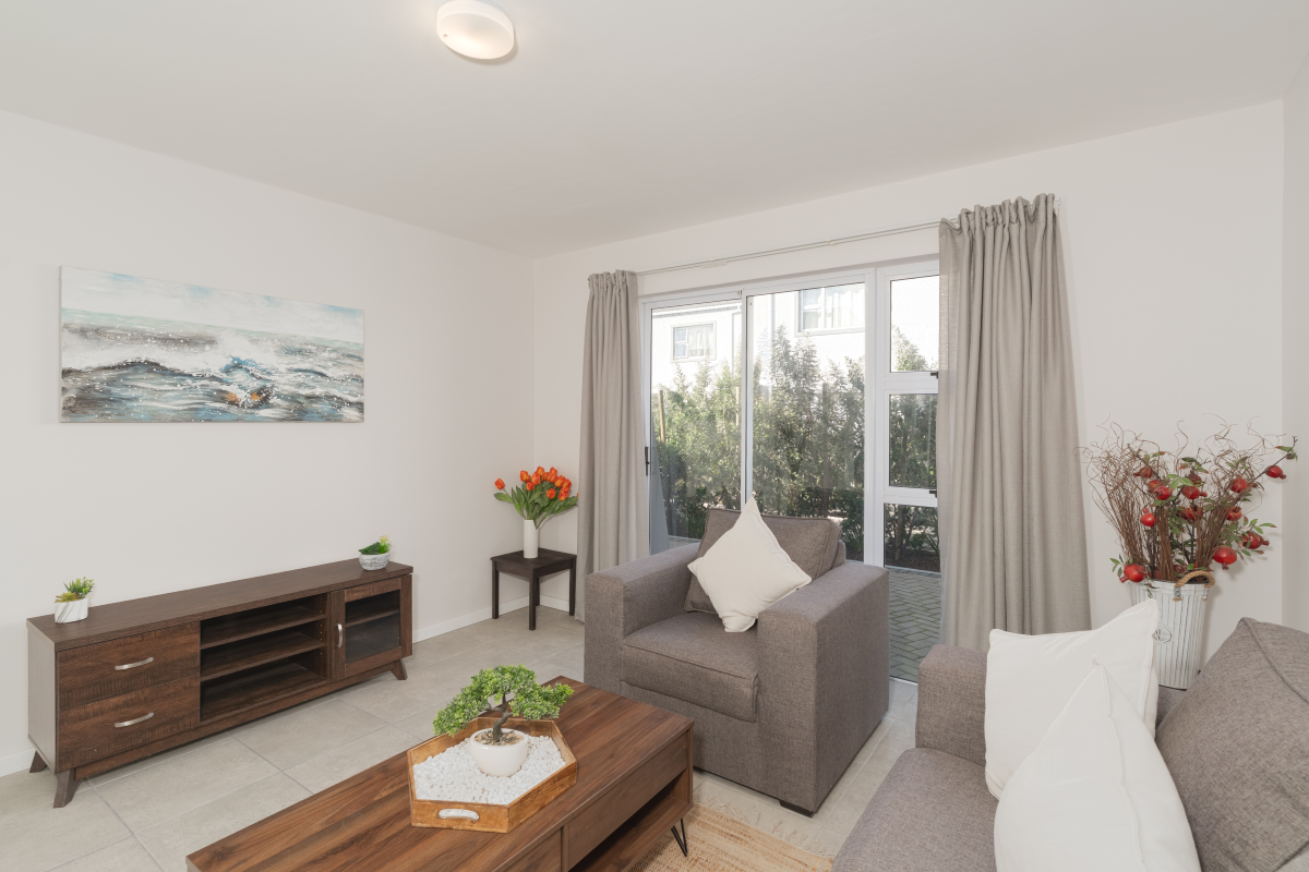 A bright living room featuring neutral tiled flooring and large sliding glass doors that provide direct access to the outdoor patio area.