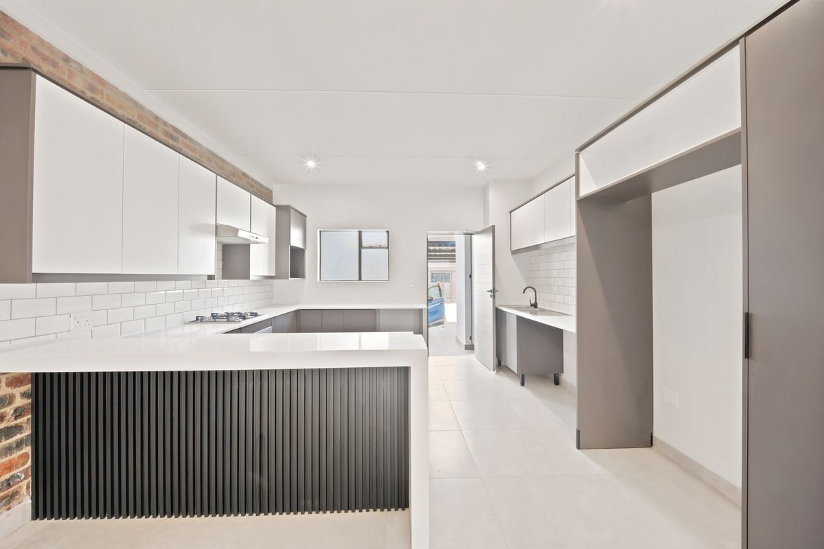 Modern kitchen featuring white cabinetry, stone countertops, a gas hob, extractor fan, and a breakfast bar with slatted detailing.