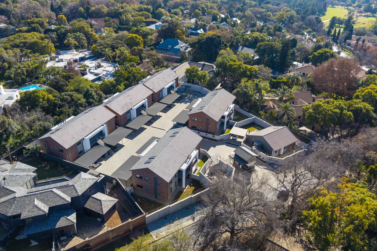 Aerial view of a modern residential apartment complex featuring multiple brick buildings, paved driveways, covered parking bays, and landscaped surroundings.