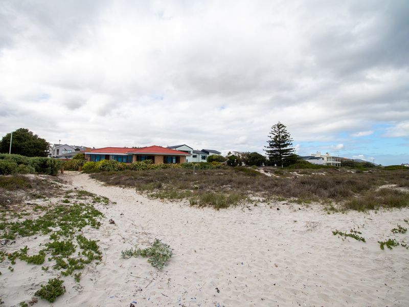 A view of the rear elevation of the house featuring a red metal roof, situated behind coastal dunes.
