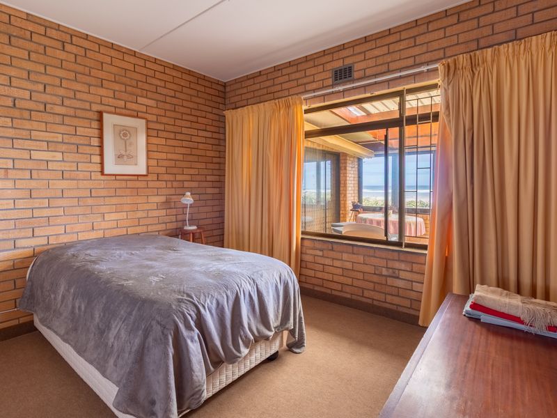 A bedroom featuring exposed brick walls, carpeted flooring, and a large window with security bars offering a view of the outdoor patio area.