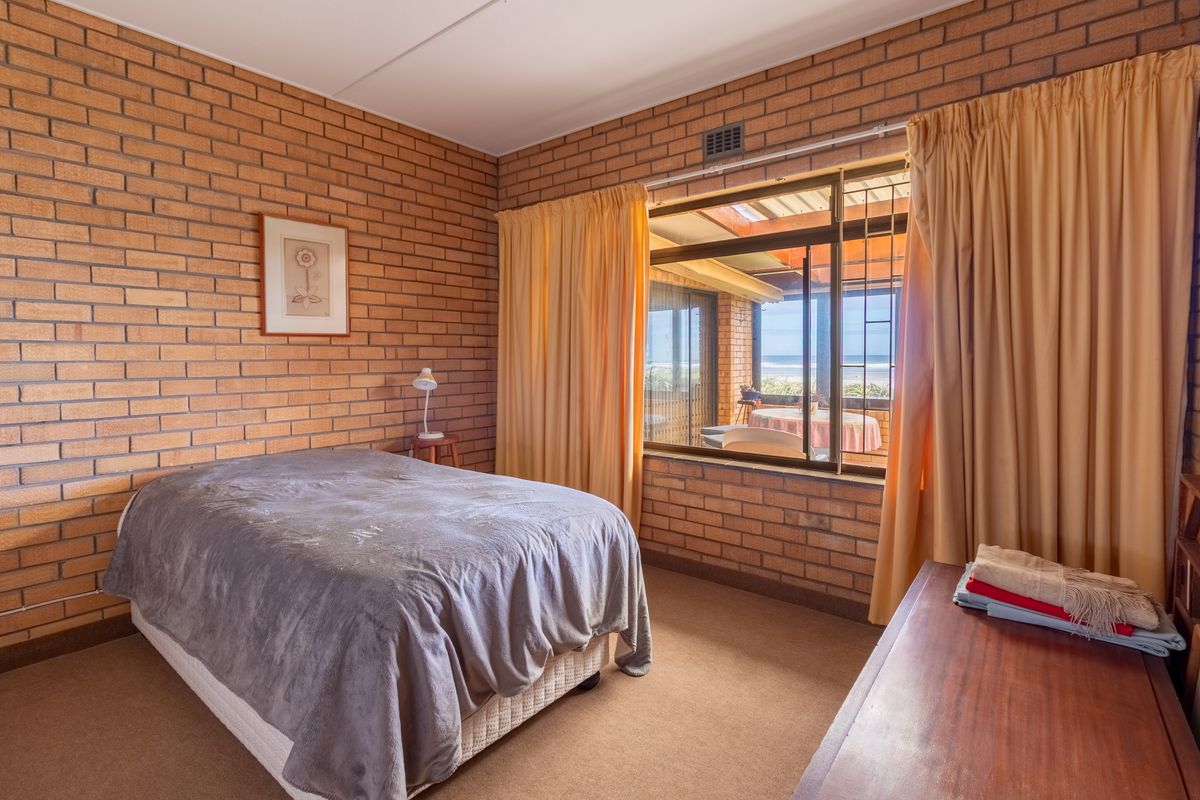 A bedroom featuring exposed brick walls, carpeted flooring, and a large window with security bars offering a view of the outdoor patio area.