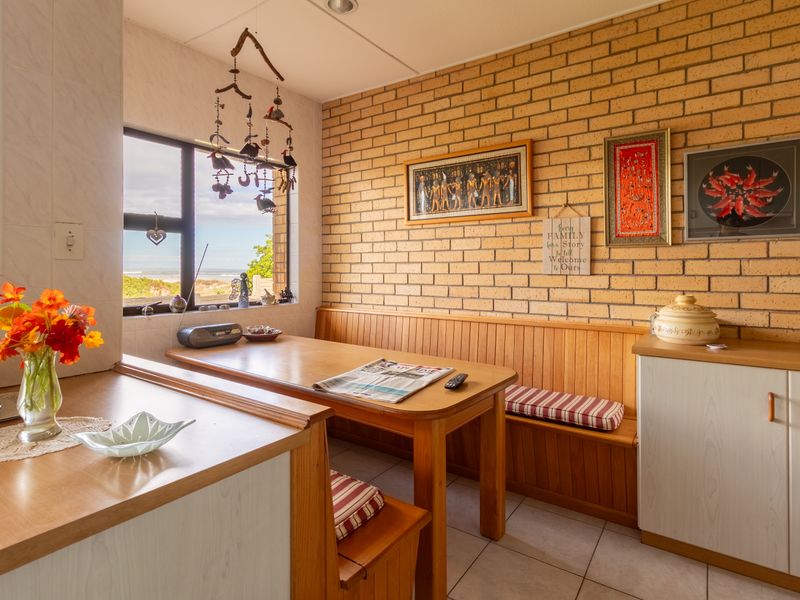 A cozy kitchen dining area featuring exposed brick walls, built-in bench seating, and a window with a view of the coast.