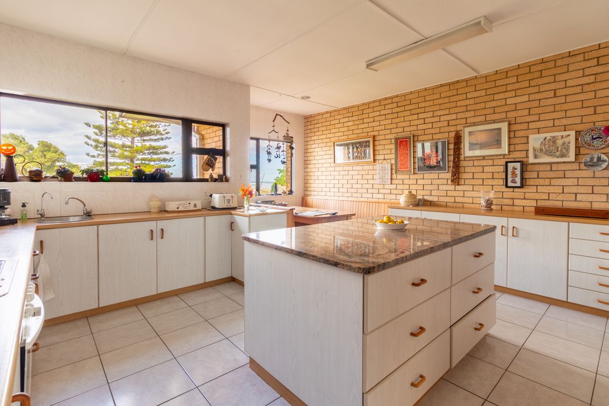 Spacious kitchen featuring a central island with granite countertop, light-toned cabinetry, tiled flooring, and an exposed brick feature wall.