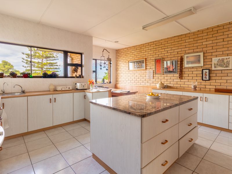 Spacious kitchen featuring a central island with granite countertop, light-toned cabinetry, tiled flooring, and an exposed brick feature wall.