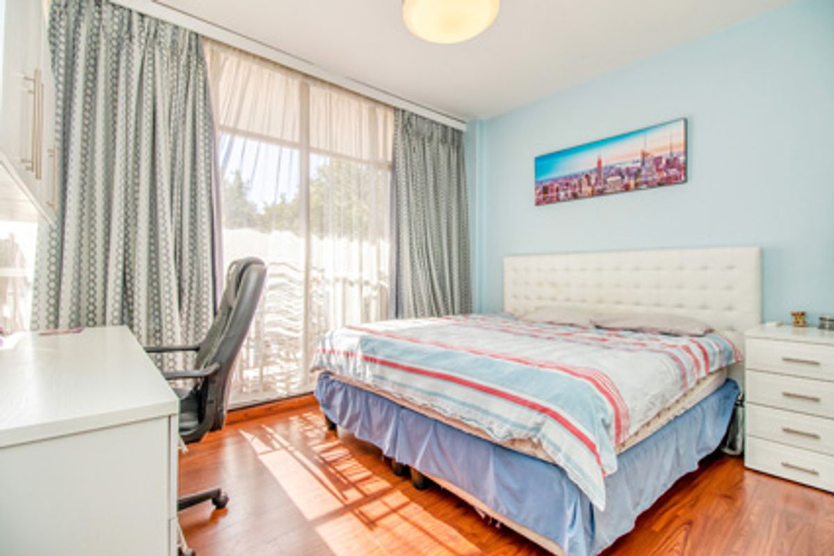 A well-lit bedroom featuring wood-look flooring, a large window with floor-to-ceiling curtains, and access to an outdoor balcony area.
