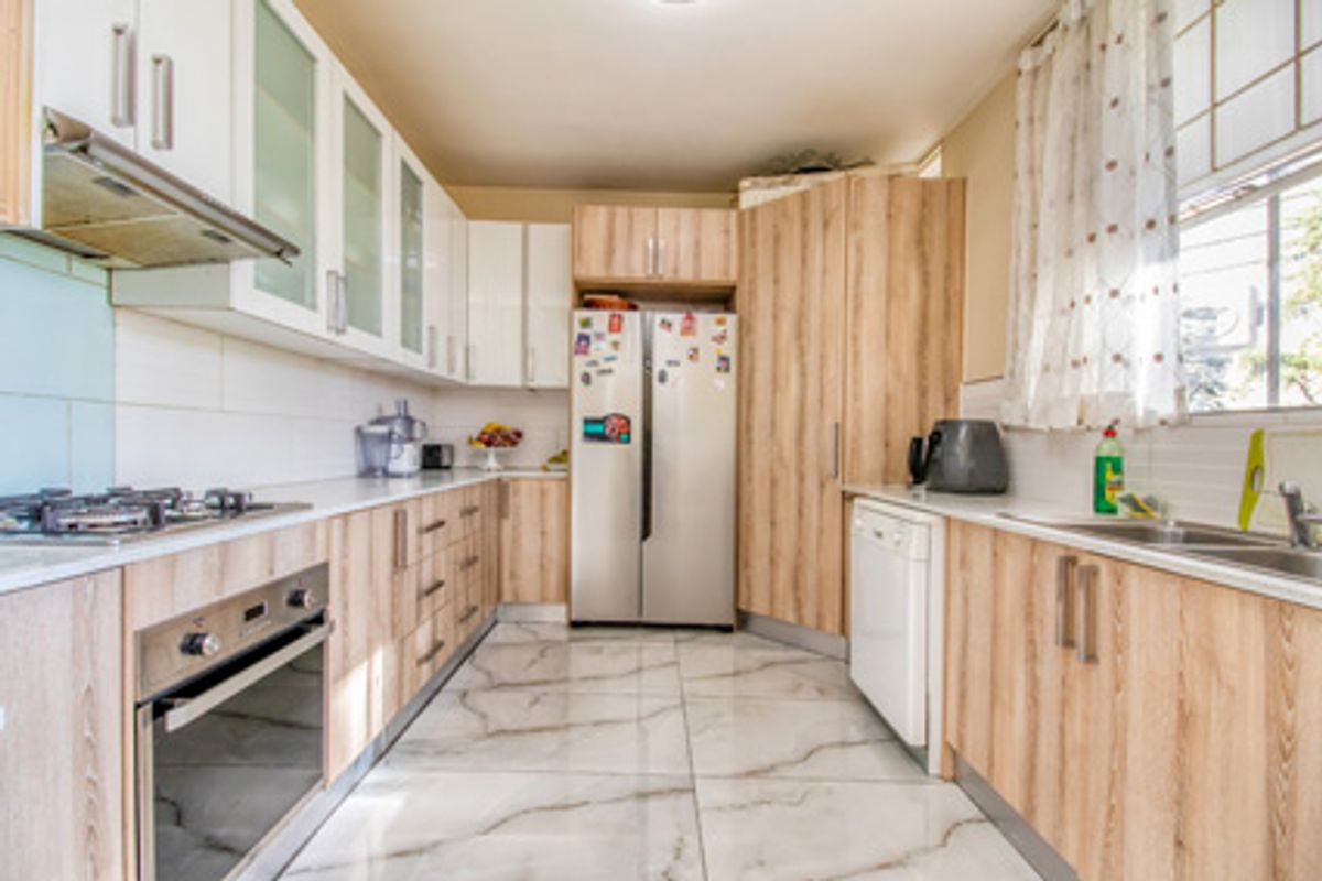 Modern kitchen featuring light wood-grain cabinetry, white upper cabinets, integrated stainless steel oven, gas hob, extractor fan, and marble-look floor tiles.