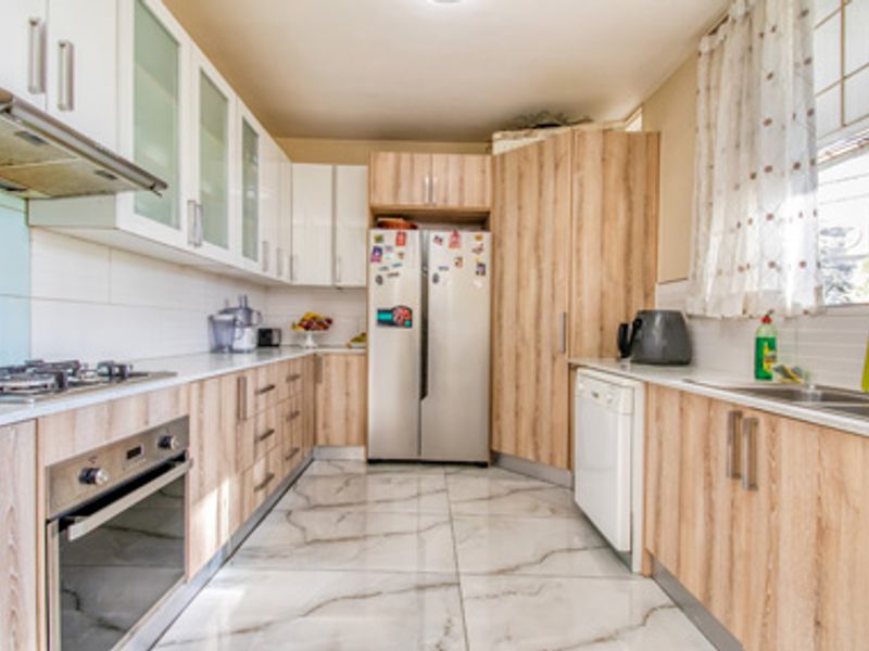 Modern kitchen featuring light wood-grain cabinetry, white upper cabinets, integrated stainless steel oven, gas hob, extractor fan, and marble-look floor tiles.
